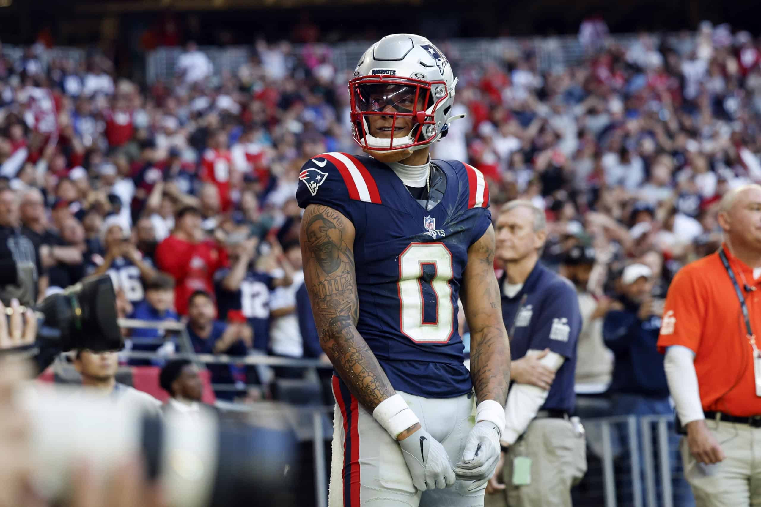 New England Patriots cornerback Christian Gonzalez walks off the field carrying his helmet while wearing his No. 0 jersey.