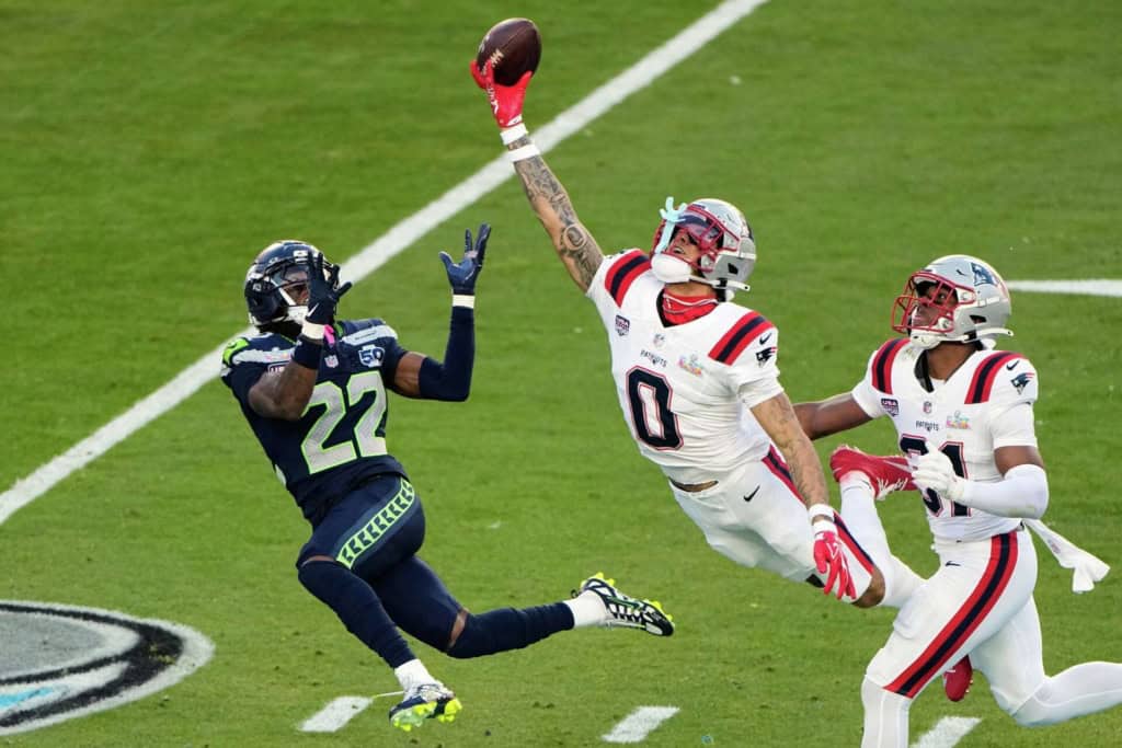 Christian Gonzalez leaps with one hand extended toward the football during a New England Patriots game against the Seattle Seahawks.