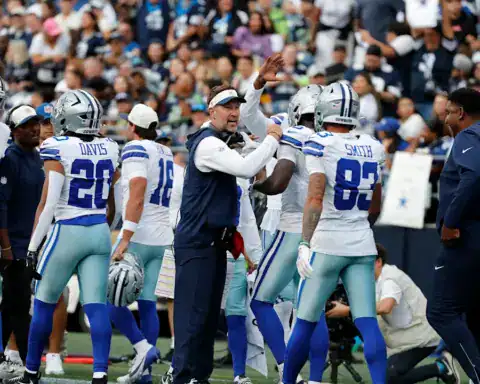 Dallas Cowboys players Malik Davis and Anthony Smith gather on the sideline with coaches during a preseason game.