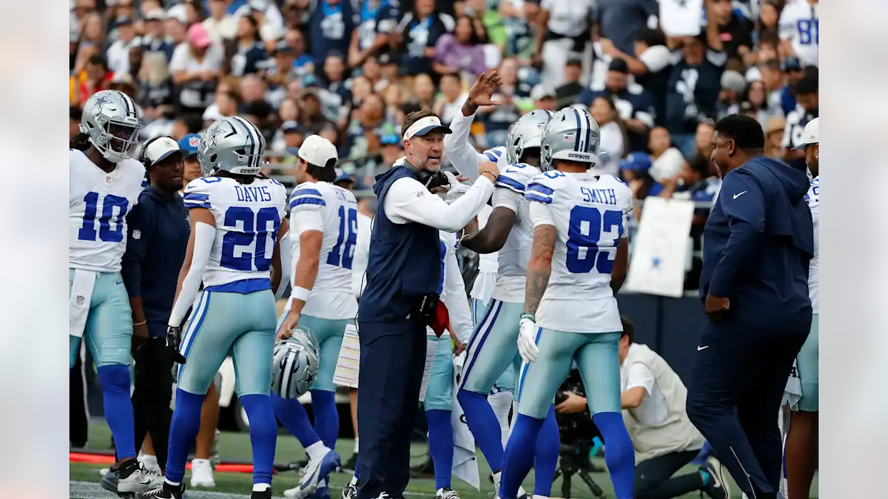 Dallas Cowboys players Malik Davis and Anthony Smith gather on the sideline with coaches during a preseason game.