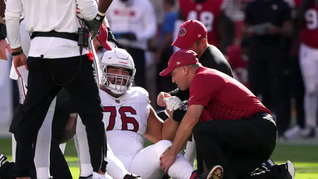 Will Hernandez sits on the field while Arizona Cardinals medical staff examine him during a game.