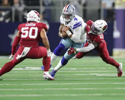 Dallas Cowboys quarterback Dak Prescott running with the football and getting tackled by two Arizona defenders.