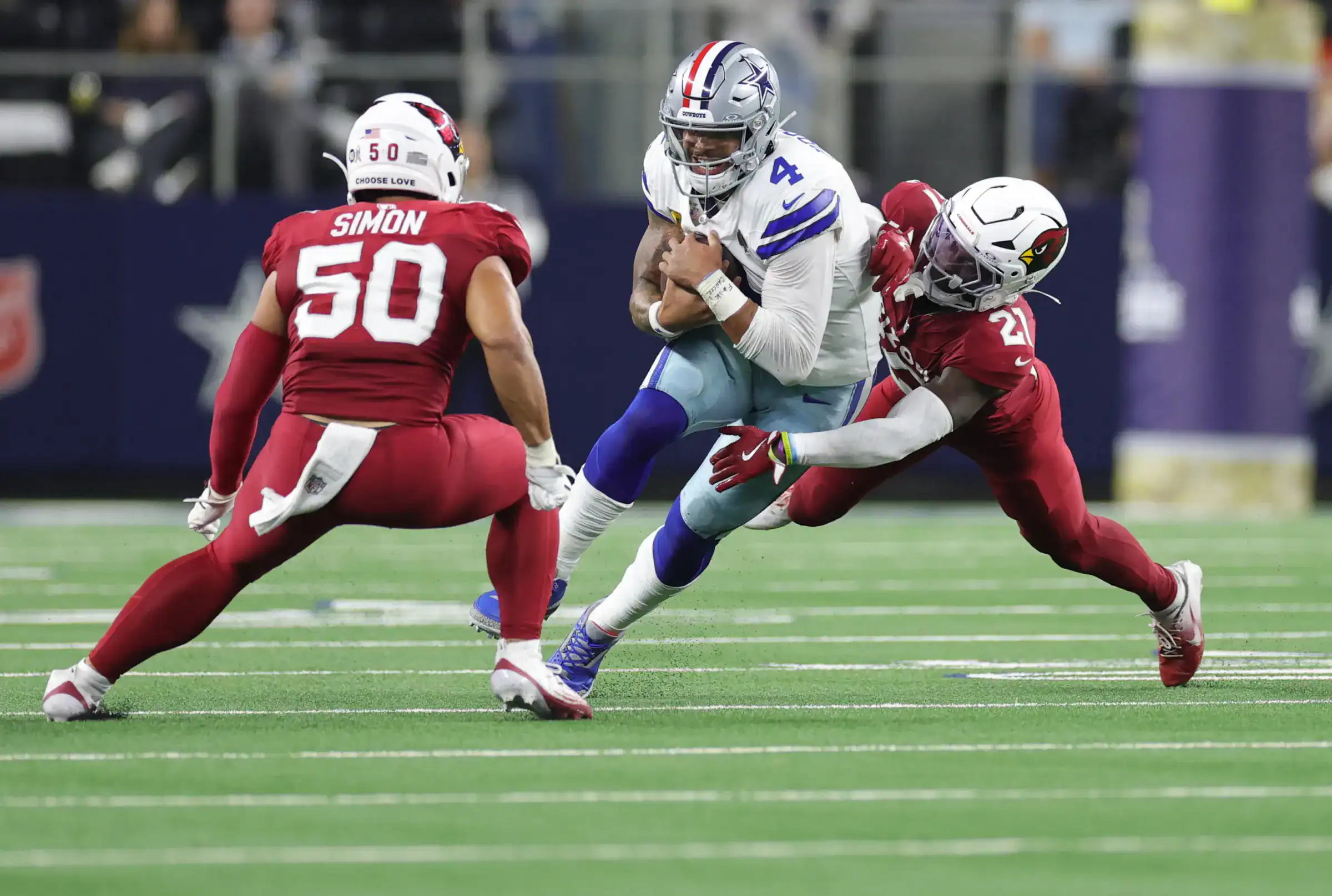 Dallas Cowboys quarterback Dak Prescott running with the football and getting tackled by two Arizona defenders.