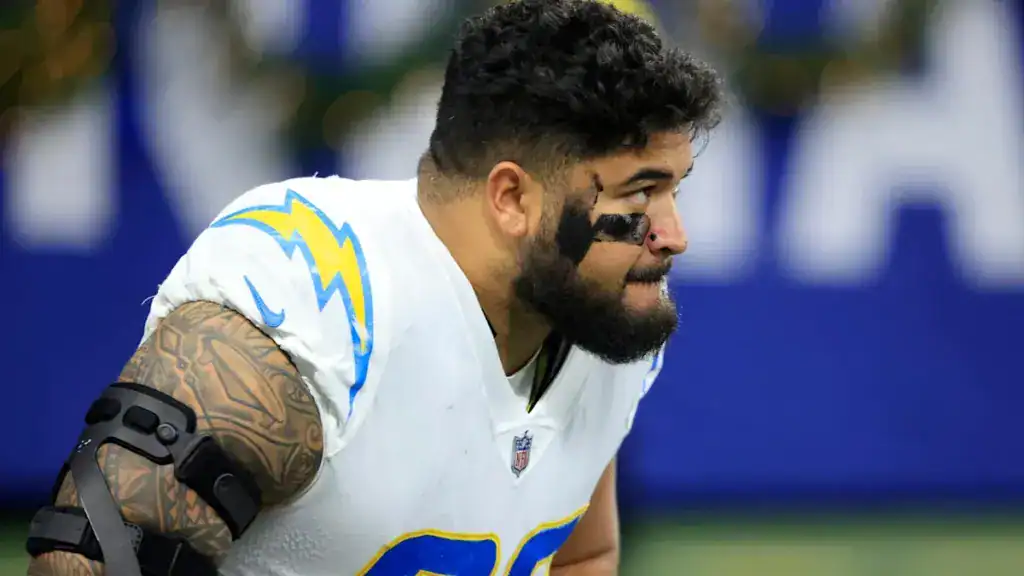 NFL lineman Breiden Fehoko kneeling on the field warming up before a game. 