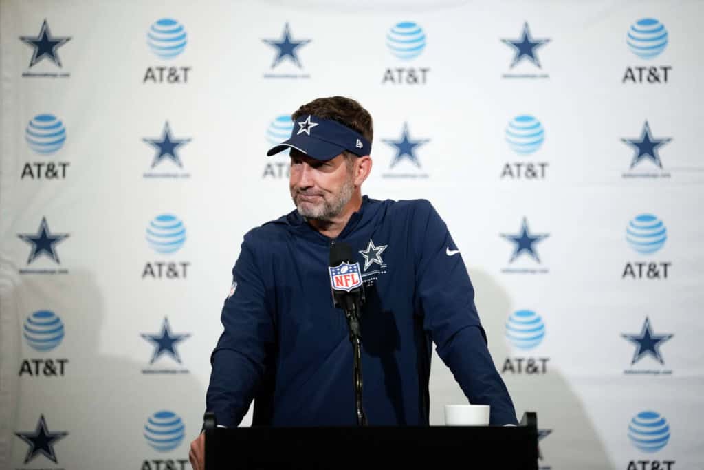 Dallas Cowboys head coach Brian Schottenheimer standing at the podium during a press conference.
