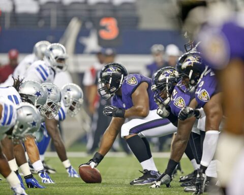American football teams in purple and white uniforms are lined up facing each other before the snap.