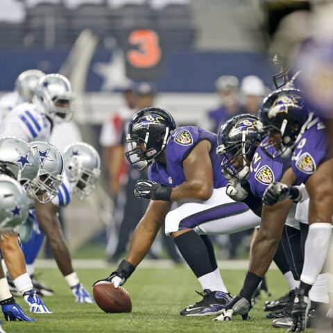 American football teams in purple and white uniforms are lined up facing each other before the snap.