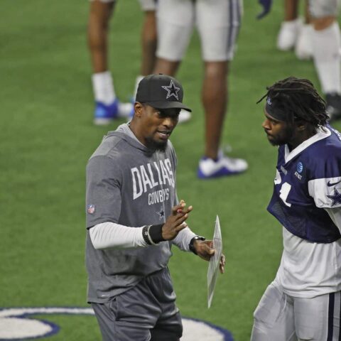 Dallas Cowboys coach in a grey outfit talks to player Trevon Diggs on the field with others in the background.