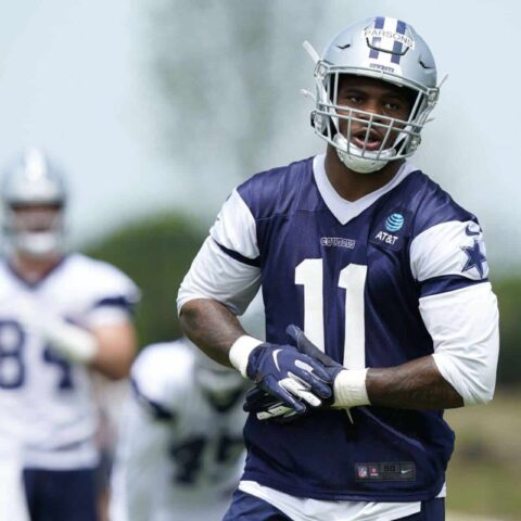 A football player in a navy and white uniform practices at Training Camp, with a teammate holding a football in the background.