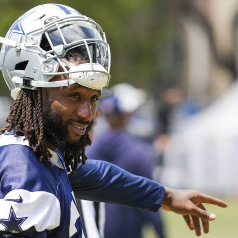 A football player in a Cowboys uniform and helmet points while standing outdoors during practice.