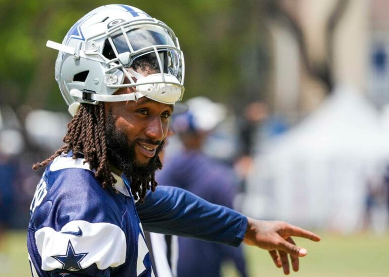 A football player in a Cowboys uniform and helmet points while standing outdoors during practice.