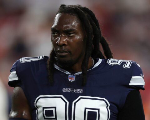 A football player in a navy blue "Cowboys" jersey with the number 90 is seen standing on the field.