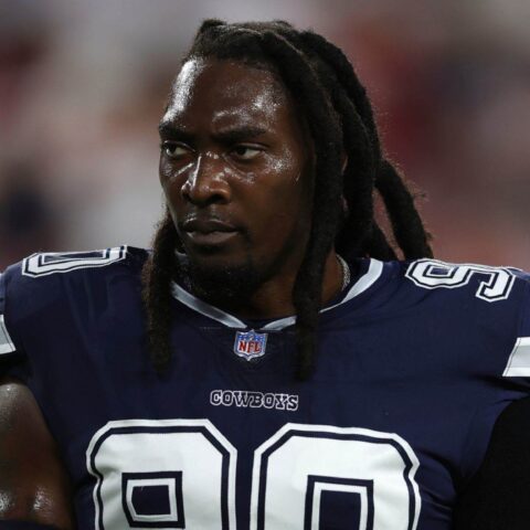 A football player in a navy blue "Cowboys" jersey with the number 90 is seen standing on the field.