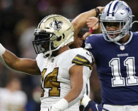 A Saints football player in a white and gold uniform celebrates while a player in a blue uniform stands in the background.