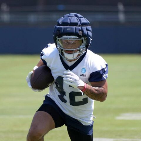 Cowboys' Deuce Vaughn, in training gear, runs with the football during a practice session on the grass field.