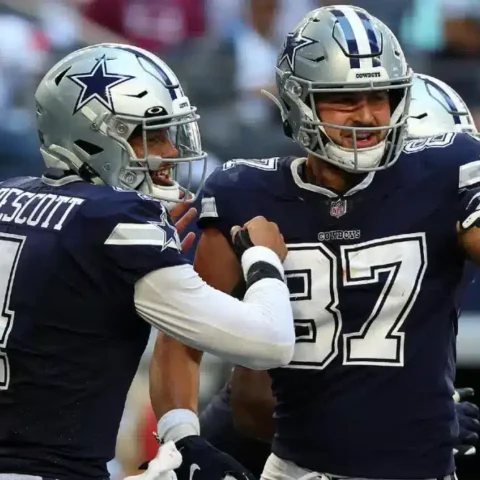 Two football players in blue uniforms celebrate on the field during a game, channeling the dynamic energy of Dak Prescott and Jake Ferguson.