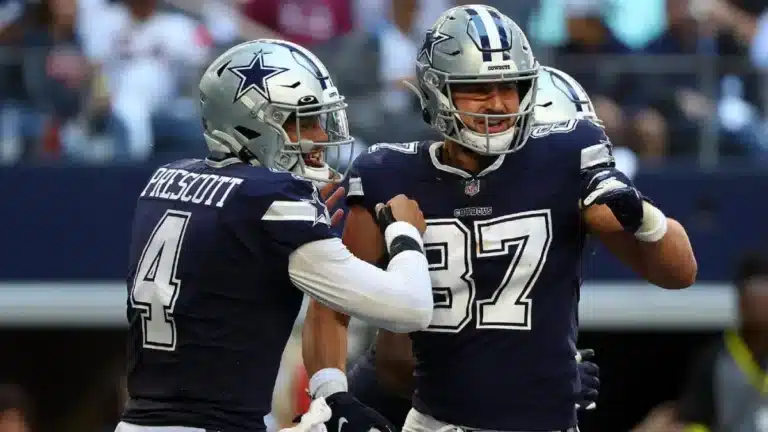 Two football players in blue uniforms celebrate on the field during a game, channeling the dynamic energy of Dak Prescott and Jake Ferguson.