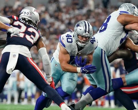 Football players from opposing teams in action during a game, with one team in blue and white uniforms and the other in blue and red. Hunter Luepke of the Cowboys makes a pivotal play that has fans on their feet.