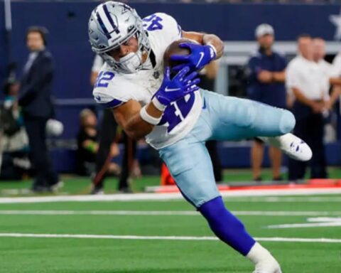 Cowboys football player Deuce Vaughn in blue and white uniform running with the ball, with defenders attempting to tackle him on the field.