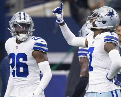 Two football players in Dallas Cowboys uniforms, including cornerback DaRon Bland, with one pointing upwards during a game.