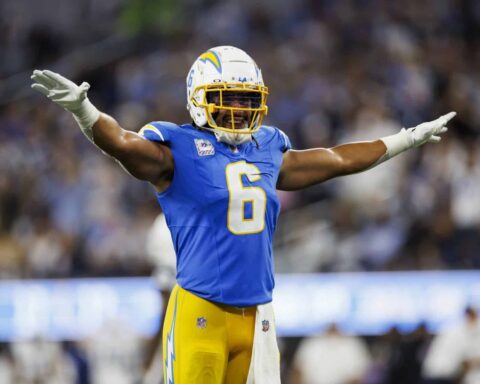 Football player in blue uniform with number 6 spreads arms wide on the field during a game. Crowd blurred in background.
