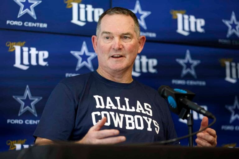 A man wearing a Dallas Cowboys shirt speaks at a press conference with a backdrop of Cowboys logos and Miller Lite branding.