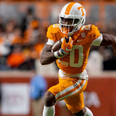 Jaylen Wright, a football player in an orange and white uniform, is seen running with the ball on the football field during a game.