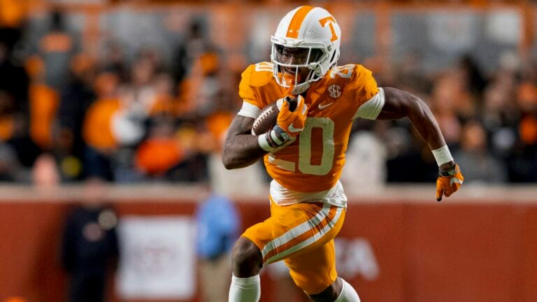 Jaylen Wright, a football player in an orange and white uniform, is seen running with the ball on the football field during a game.