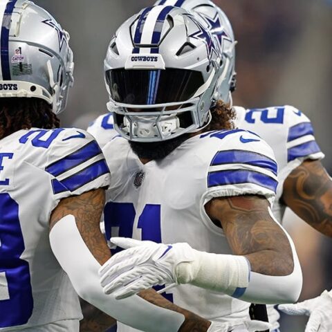 Two football players in Cowboys uniforms, numbered 23 and 21, embrace on the field.