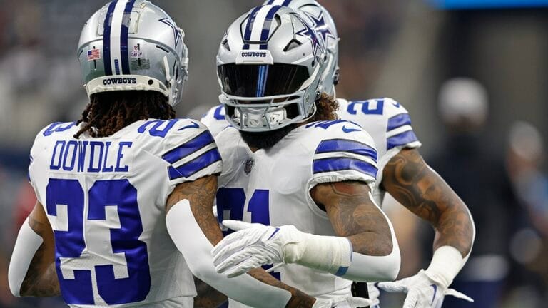 Two football players in Cowboys uniforms, numbered 23 and 21, embrace on the field.