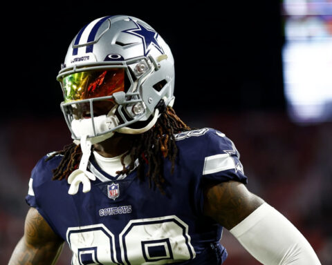 Football player in a Dallas Cowboys uniform and helmet stands on the field during a game.