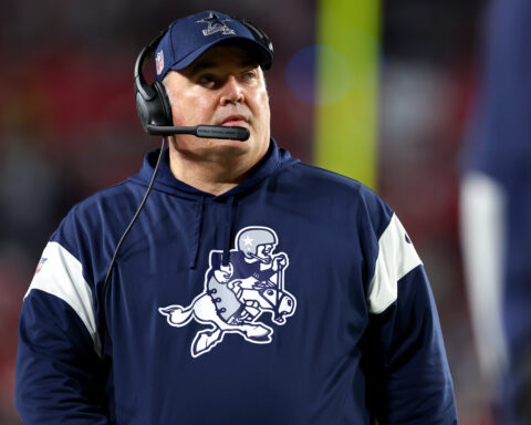A dedicated coach in a navy sports hoodie and headset attentively observes the game, strategizing every move.