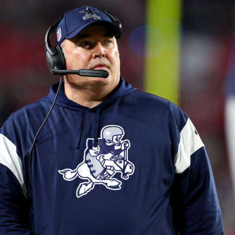 A dedicated coach in a navy sports hoodie and headset attentively observes the game, strategizing every move.