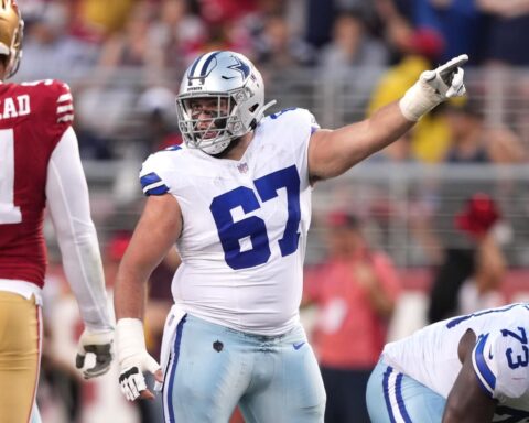 Dallas Cowboys player in a white uniform points during a game against the San Francisco 49ers, signaling to teammate Brock Hoffman.
