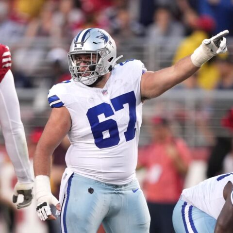 Dallas Cowboys player in a white uniform points during a game against the San Francisco 49ers, signaling to teammate Brock Hoffman.