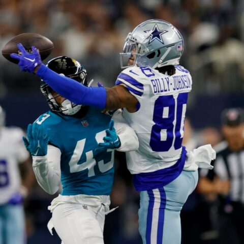 A football player in a blue uniform attempts to catch a pass, while Tyron Billy-Johnson, in a white and blue uniform, tries to block him.