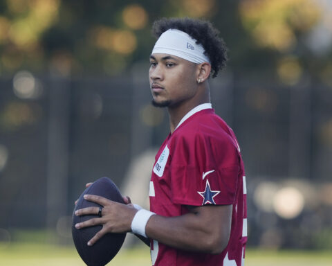 A football player in a red jersey holds a football, standing outdoors with a focused expression.