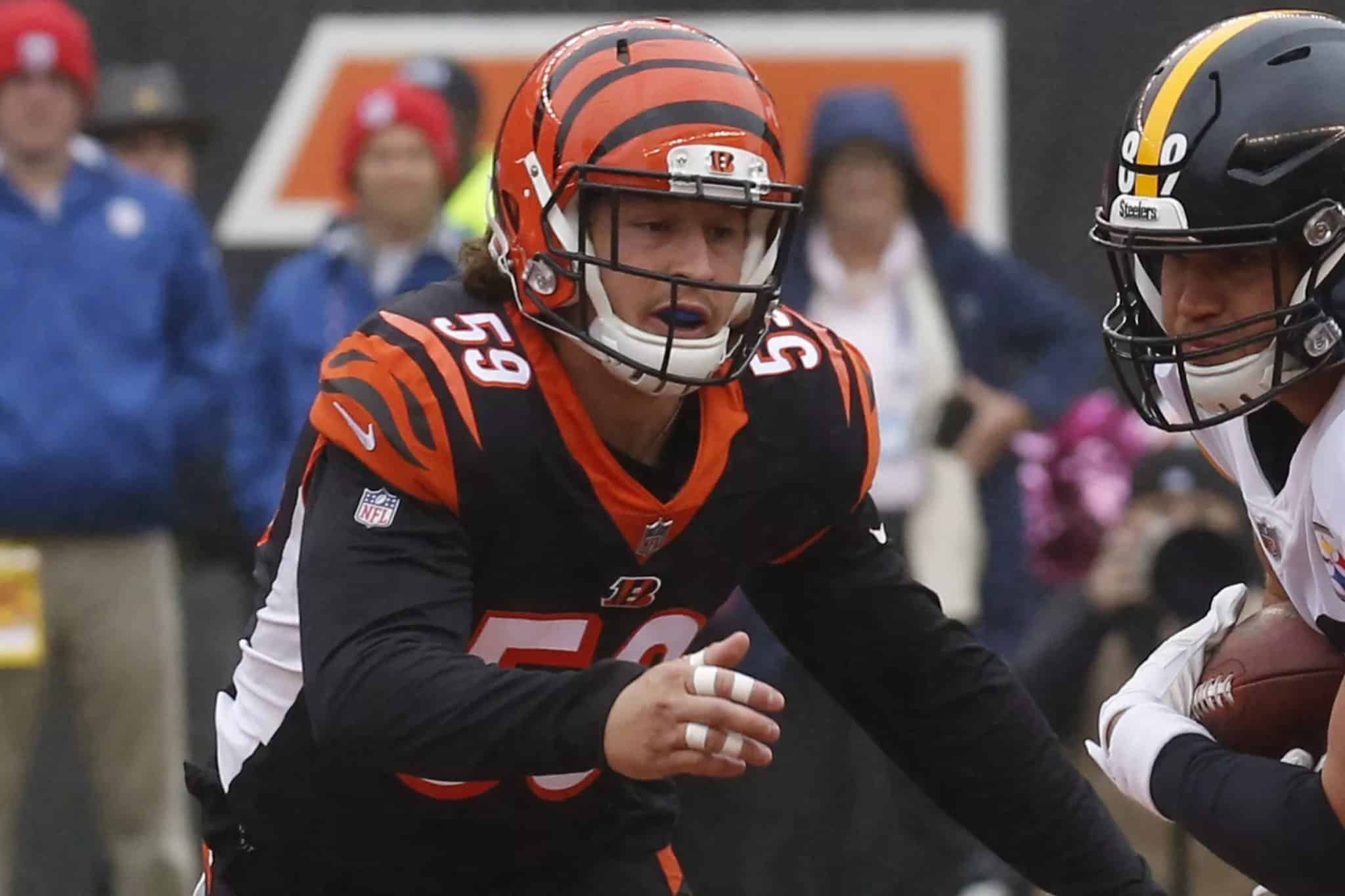 Football player in a Cincinnati Bengals jersey reaches out during a game against an opposing player in a black and yellow uniform.