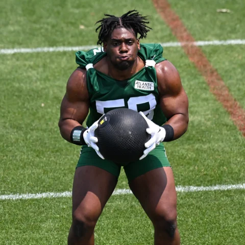 A football player wearing a green jersey holds a medicine ball during a training session on a grass field.