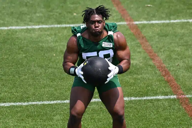 A football player wearing a green jersey holds a medicine ball during a training session on a grass field.