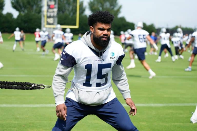 Football player training on a field with teammates in the background during a practice session.