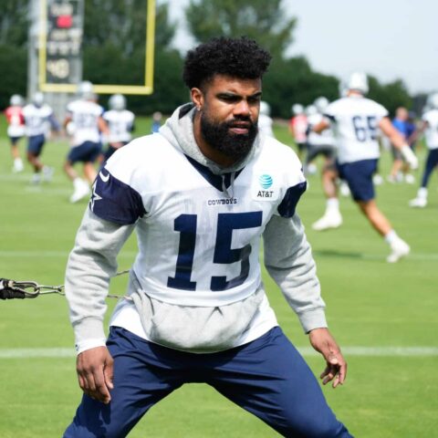 Football player training on a field with teammates in the background during a practice session.
