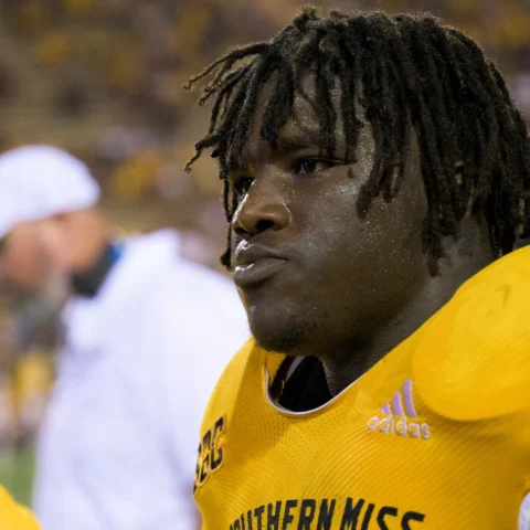 A football player in a yellow "Southern Miss" jersey stands on the sidelines during a game.