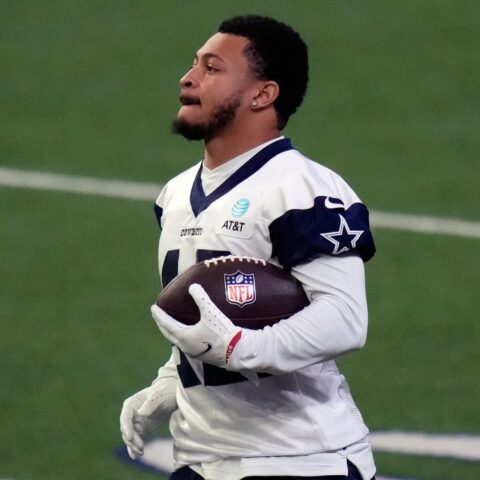 A football player in a white jersey holding a football on a field during a practice session.