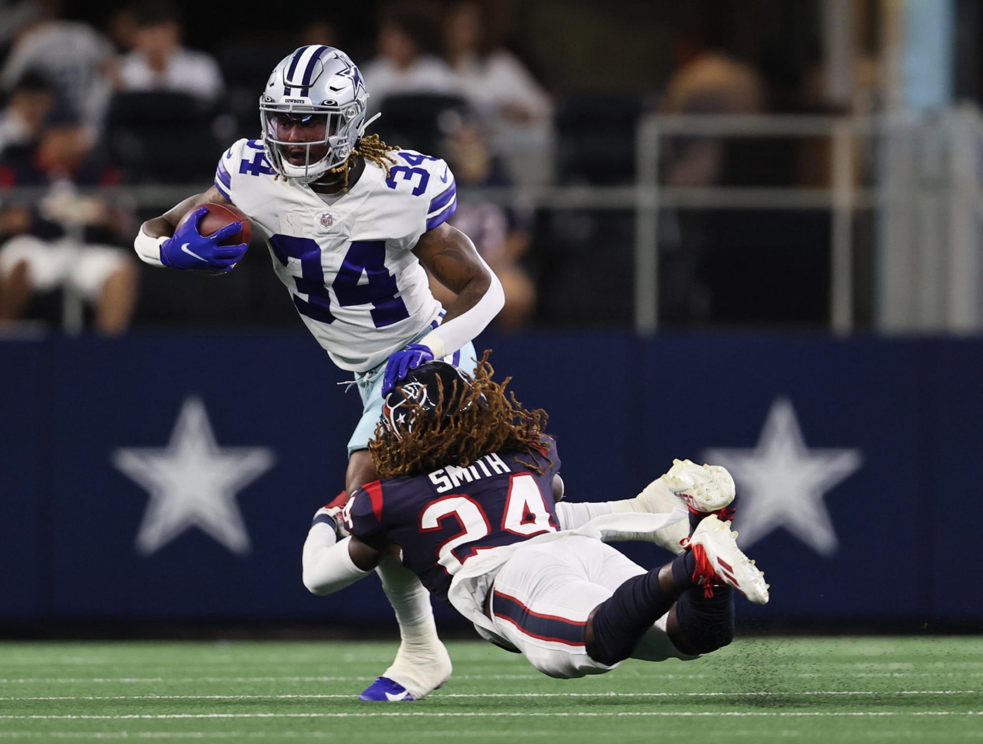 Football player in a white jersey runs with the ball while a player in a black jersey dives to tackle him.