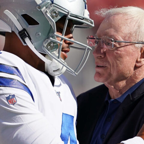 A football player in uniform and a man in a suit embrace on the field.