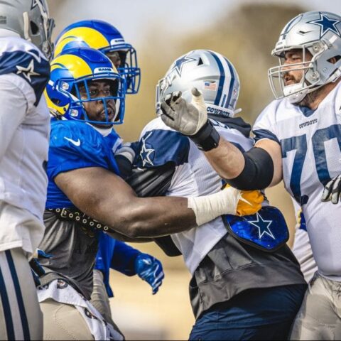 Football players from two teams in blue, white, and yellow uniforms engaged in a heated altercation during a Cowboys vs Rams practice game.
