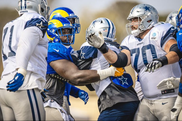 Football players from two teams in blue, white, and yellow uniforms engaged in a heated altercation during a Cowboys vs Rams practice game.