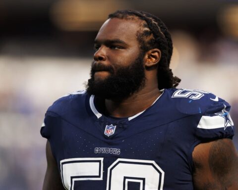 A football player in a Dallas Cowboys jersey stands on the field with a focused expression.