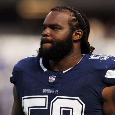A football player in a Dallas Cowboys jersey stands on the field with a focused expression.